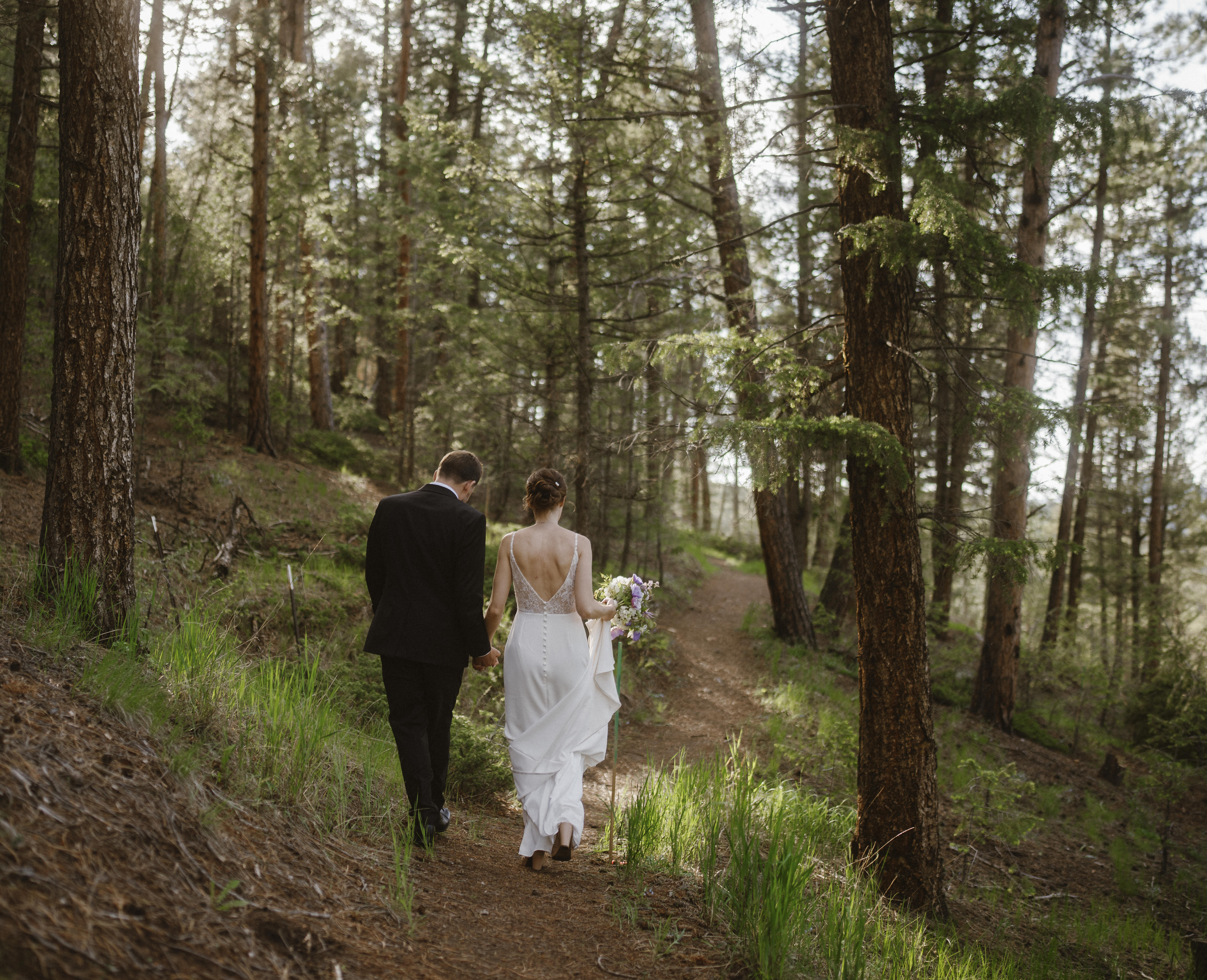 Eva & Dan walk hand in hand through the woods in Evergreen Colorado after their wedding ceremony at Juniper Lodge & Treehouses.