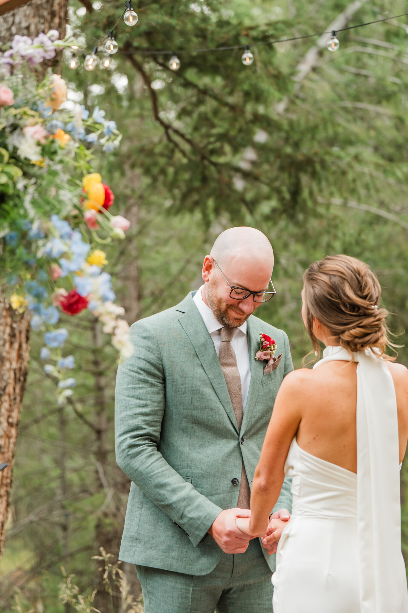 Wedding under bright wildflower arch during outdoor ceremony in the meadow at Juniper Lodge & Treehouses.