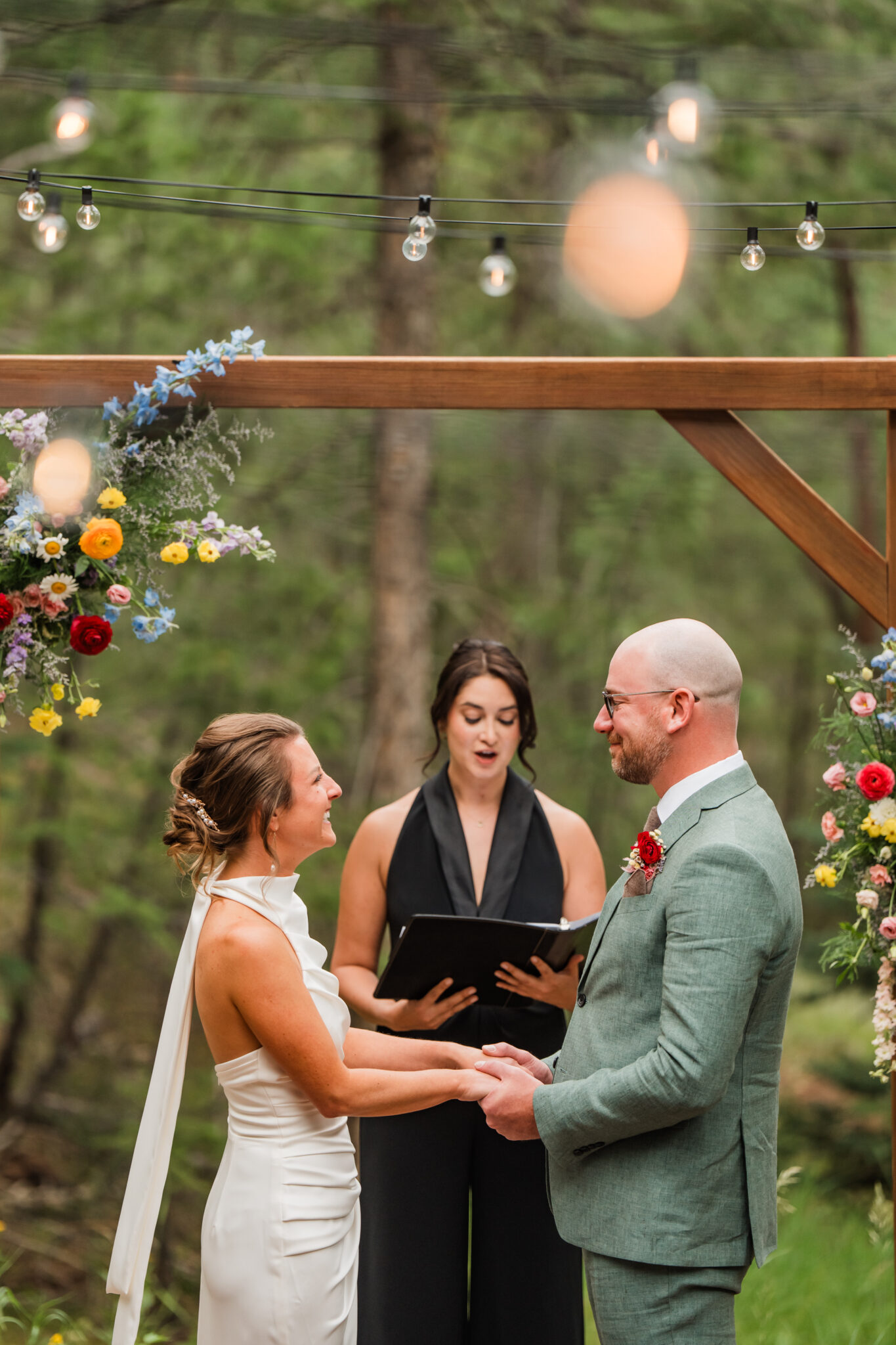 Wedding under bright wildflower arch during outdoor ceremony in the meadow at Juniper Lodge & Treehouses.