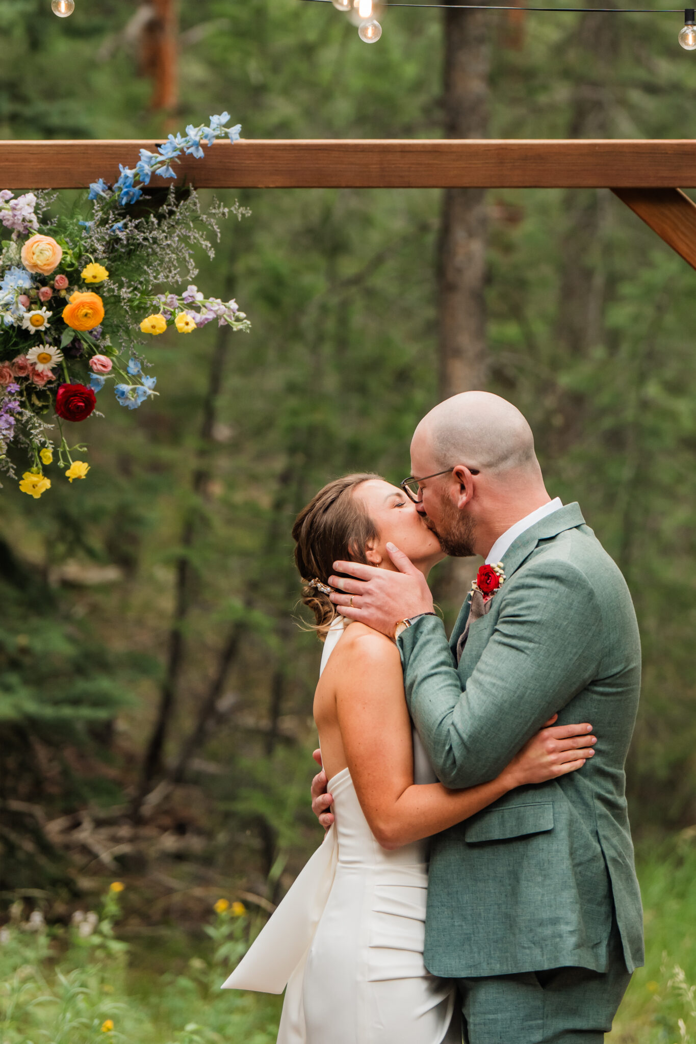 First kiss under bright wildflower arch during outdoor ceremony in the meadow at Juniper Lodge & Treehouses.