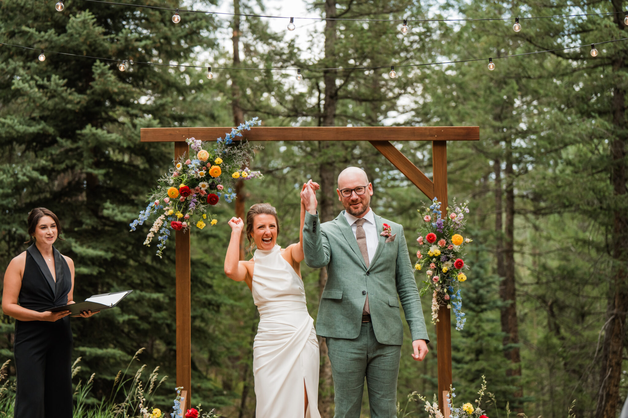 Wedding under bright wildflower arch during outdoor ceremony in the meadow at Juniper Lodge & Treehouses.